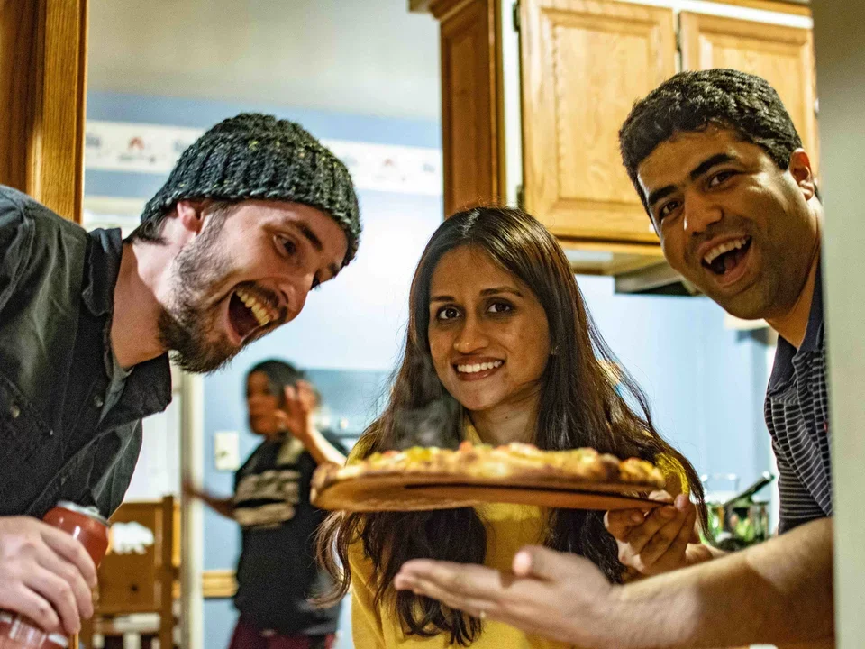 Negin holding up the handmade fresh baked pizzas to two other lab members, March 2019.