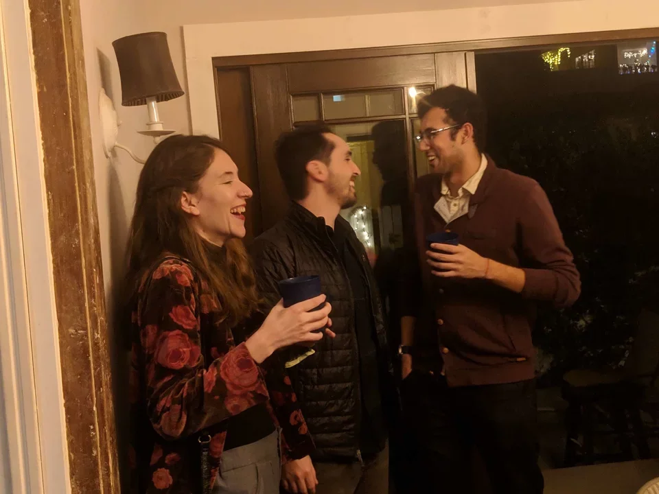Anya, Matt, and Humza standing and talking at holiday party, Dec 2018