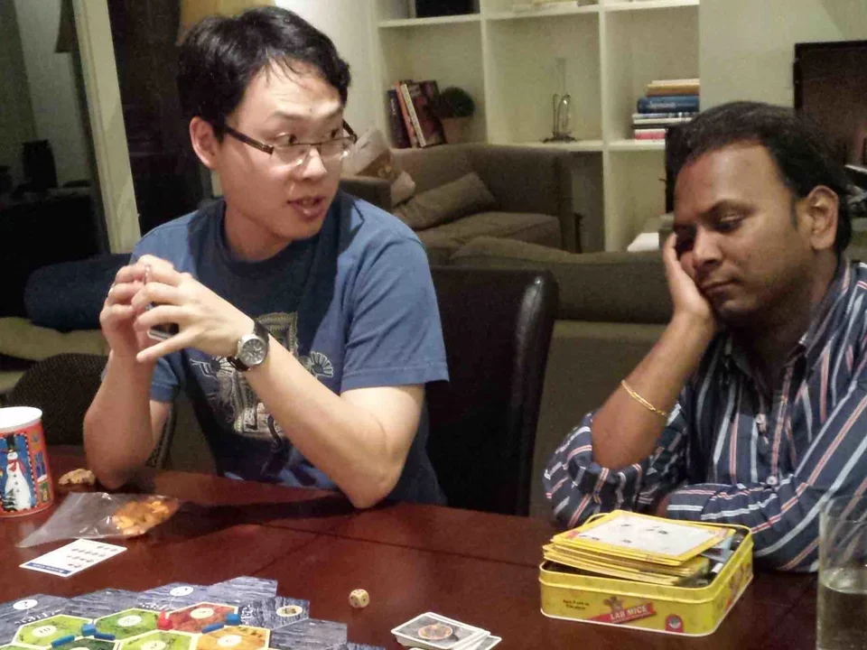 Two men, Andrew and Vivek, sit at table and play card game on  Mar 15, 2014.